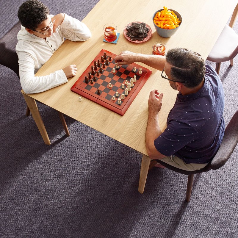 father and son playing chess and eating snack in a living room with purple carpet from Carpet Depot Inc in the North Hollywood, CA area